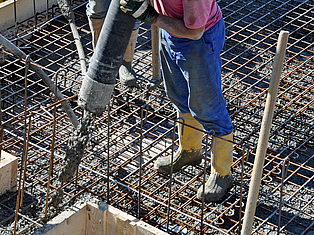 Bauarbeiter füllt flüssigen Beton mit einem Schlauch in eine Stahlbewehrung.