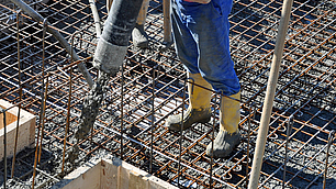 Bauarbeiter füllt flüssigen Beton mit einem Schlauch in eine Stahlbewehrung.